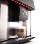 Coffee machine dispensing a latte into a glass.