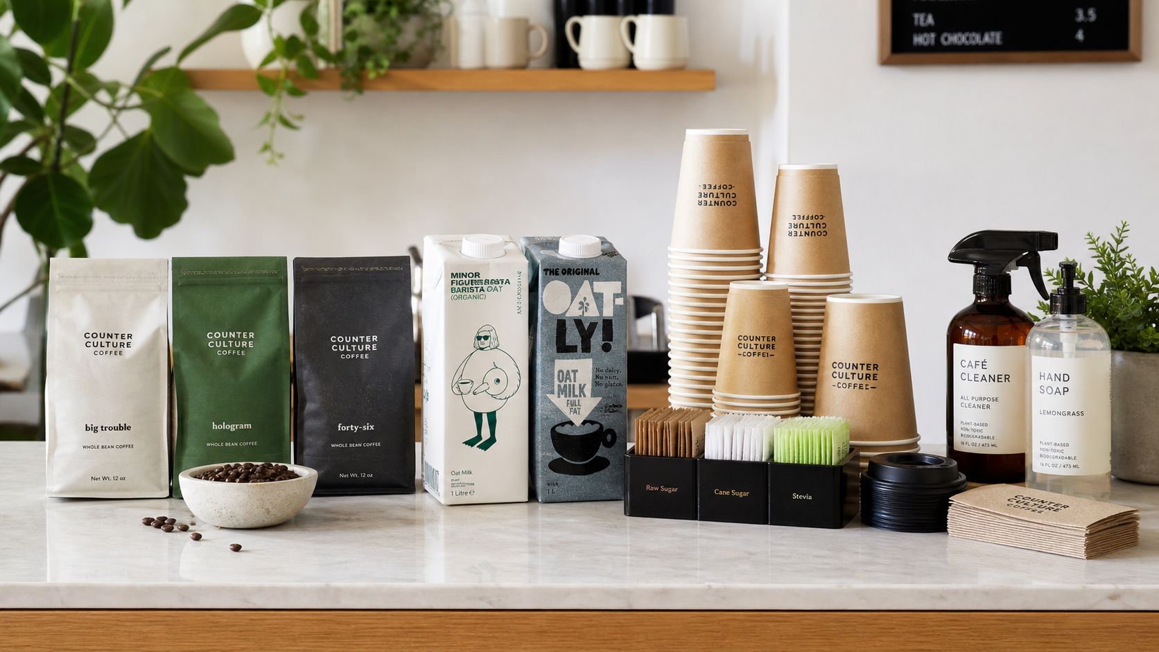 A counter with coffee beans, oat milk, paper cups, sugar packets, cleaner, and soap for a café.