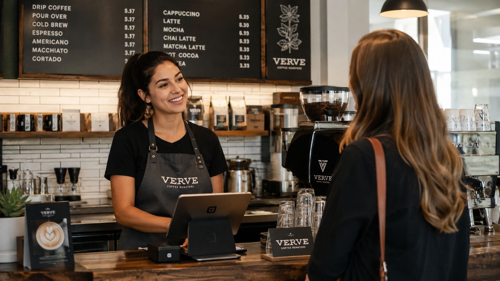 A smiling barista wearing a branded Verve Coffee Roasters apron takes an order from a customer.